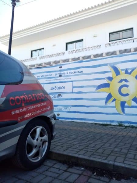 Vinil aplicado em tapumes na Comporta, com design de listras azuis e amarelas.