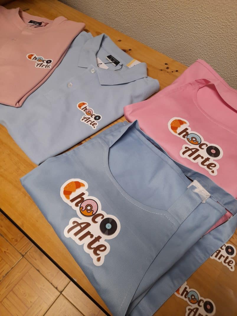 Imagem de fardas personalizadas com o logotipo ChocoArte em cores pastel.