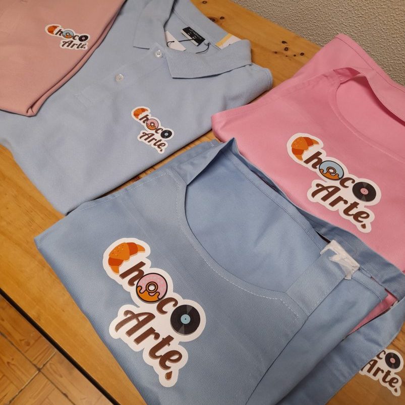 Imagem de fardas personalizadas com o logotipo ChocoArte em cores pastel.